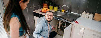 A person kneeling on the floor next to a person in a kitchen