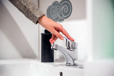 Close-up of a hand turning off a sleek chrome faucet, with a minimalist bathroom aesthetic in the background. Leaky faucets can waste gallons of water, but with a few simple tools and guidance, homeowners can often fix them on their own.