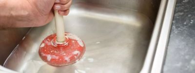 Technician using plunger to clear a clogged sink - Thomas & Galbraith Heating, Cooling, & Plumbing