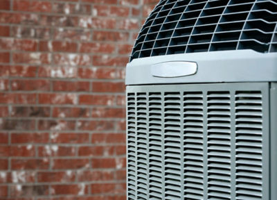 An image of an outdoor AC unit in front of a brick wall