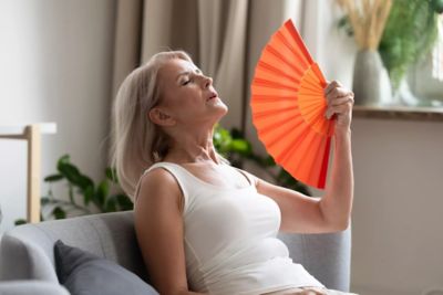 Image of a woman sitting on a couch fanning herself with a handheld fan