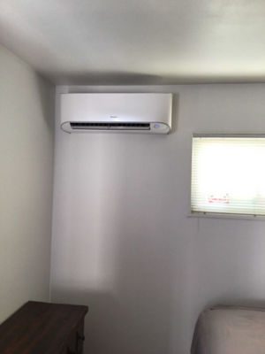 A ductless ac mounted on a wall in a bedroom.