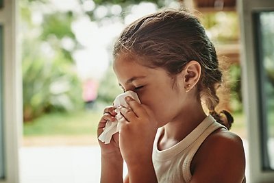 Image of kid sneezing into a tissue in front of a window