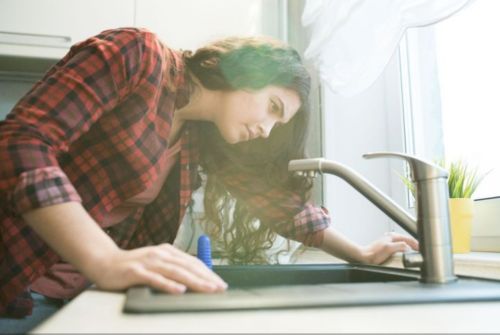 Woman leaning over her kitchen sink, looking at the faucet