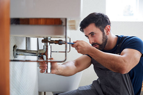 Male Plumber Using Wrench To Fix Leaking Sink 