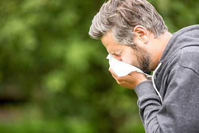 Man sneezing into tissue outside