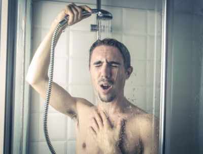 Man holding shower head above looking suprised and cold