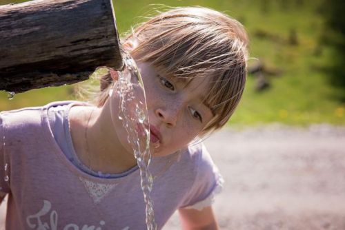 Girl drinking running water coming out of a brown tree log