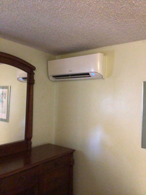 A ductless ac mounted on a wall in a bedroom.