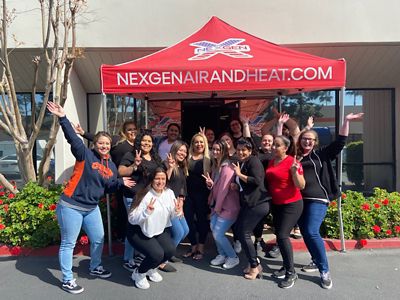 Group of people standing under a nNexGen booth giving peace signs