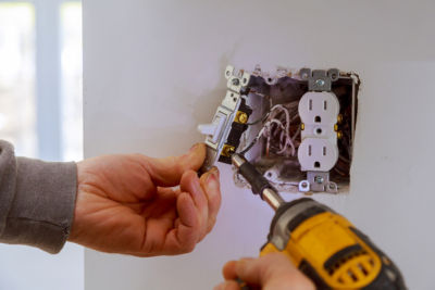 The hands of an electrician installing a power switch to the electrical junction box