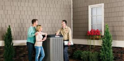 An image of a couple standing outsdie of a house with a technician over a Lennox AC unit