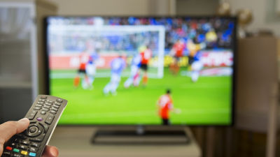 Hand holding remote up to flat screen with soccer match showing on display