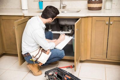 Plumber looking under kitchen sink writing down findings