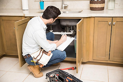 Plumber looking under kitchen sink writing down findngs