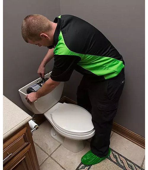 Plumber performs maintenance on a toilet tank 