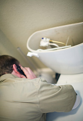 Plumber talking on phone while leaning on broken toilet