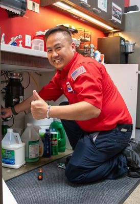 Smiling plumber working under sink giving a thumbs' up