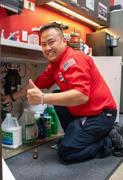 Smiling plumber working under sink giving a thumbs' up