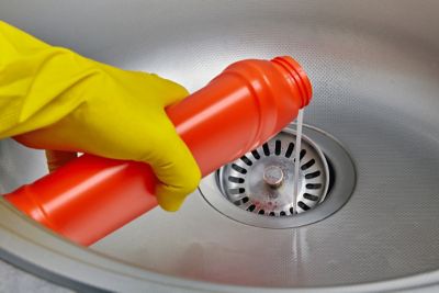 An image of a hand wearing a yellow rubber glove pouring drain cleaner down the sink