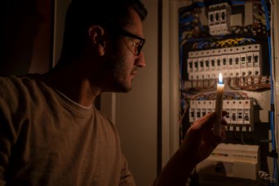 Guy holding a candle in the dark checking out his electrical panel to see why his power went out