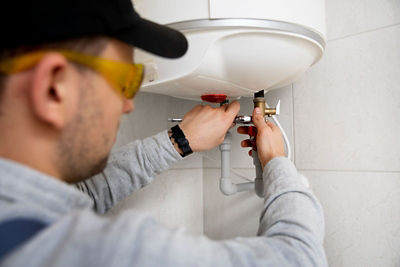 A professional technician repairing a water heater, carefully adjusting pipes and connections. Hidden water leaks, often unnoticed, can lead to significant damage over time.