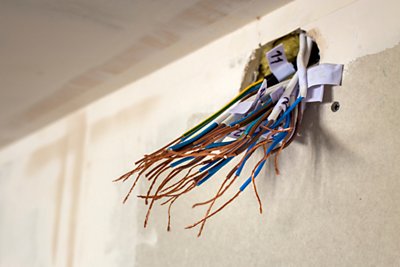 Electrical exposed connected wires protruding from socket on white wall. Electrical wiring installation. Finishing works in renovated apartment.