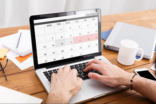 Open laptop on a wood desk showing a digital calendar on screen