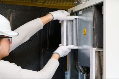 A tech wearing all white, replacing an air filter on a furnace