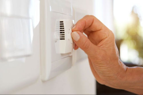 A right hand adjusting the dial on a white thermostat