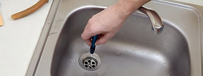 Someone using a screwdriver to remove a drain from a sink