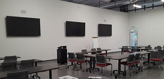 Training facility with flat-screen TVs, podium, tables, and chairs.