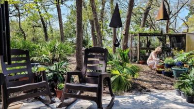 A seating are in a tree filled backyard with a woman gardening 