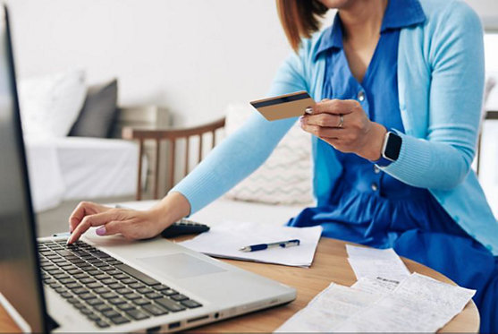 Woman wearing blue dress paying bills online on her laptop 
