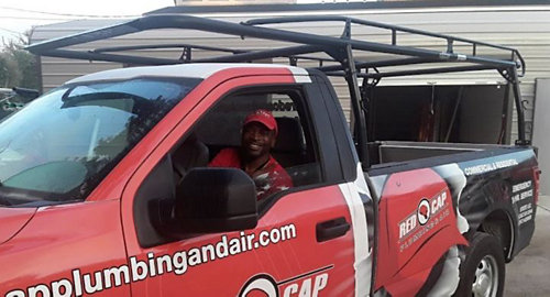 Red Cap Plumbing & Air tech smiling in a branded service truck