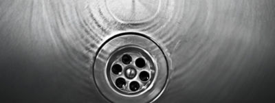 Closeup of a drain in a steel sink with water running in it 