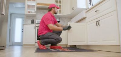 Uniformed Red Cap tech looking under a kitchen sink cabinet