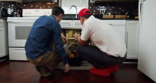 Uniformed tech looking under the sink with a customer