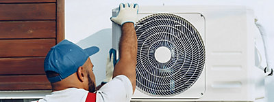 A person in overalls and blue hat working on an air conditioner