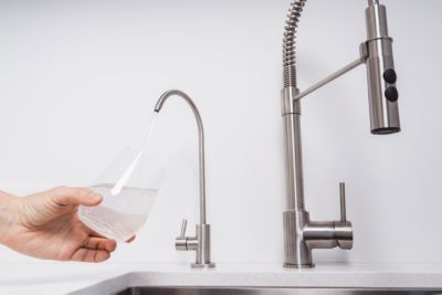 Woman get filtered water from stainless faucet into a glass