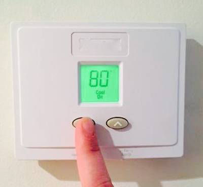 Finger on white thermostat adjusting temperature