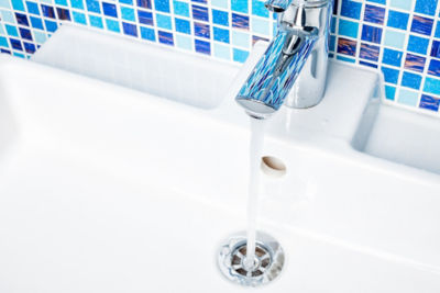 Water pouring from faucet with blue tiles in background