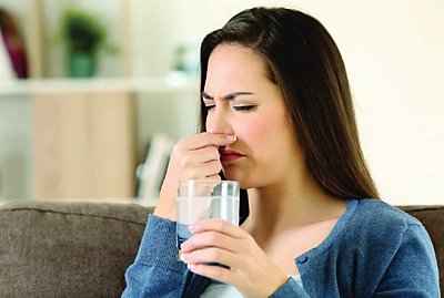 Woman holding a cup of water and holding her nose shut.