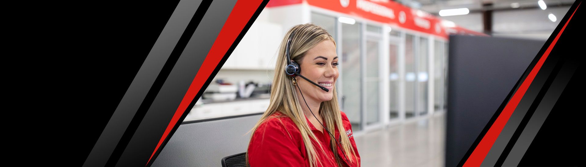 A smiling Red Cap service tech wearing a headset and sitting at a computer