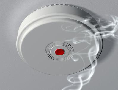 Smoke detector on the ceiling with smoke in front of it.