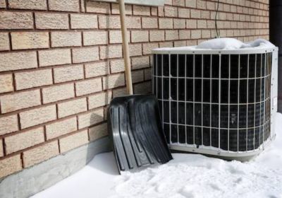 Snow shovel sitting next to outdoor unit with brick wall behind