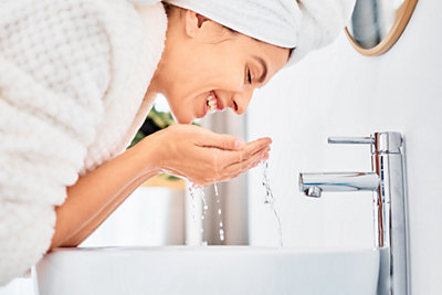 woman at her home, splashing water on her face during skincare routine