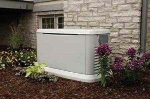 Standby generator sitting outside a brick home with flowers next to it
