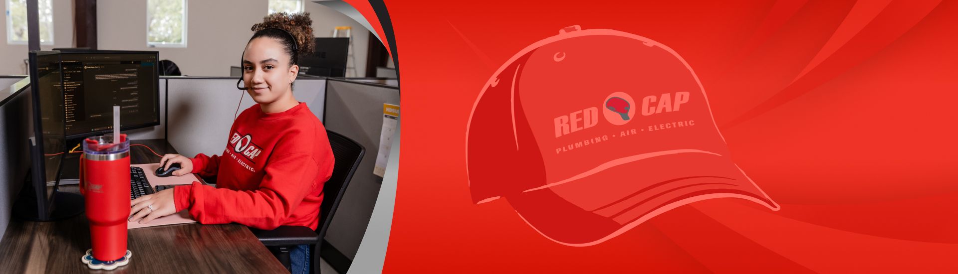 A smiling Red Cap service tech wearing a headset and sitting at a computer