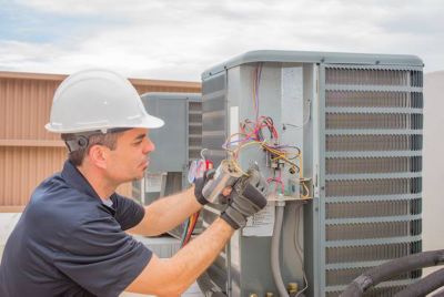 Technician checking wires on air conditioning unit outside